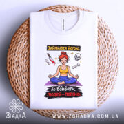 Футболка йога чорний гумор, біла, складена на плетеній основі, фон світло-сірий, принт з дівчиною в позі йоги, червоним волоссям, жовтою майкою та синіми штанами, навколо малюнка кістки, ніж та череп.