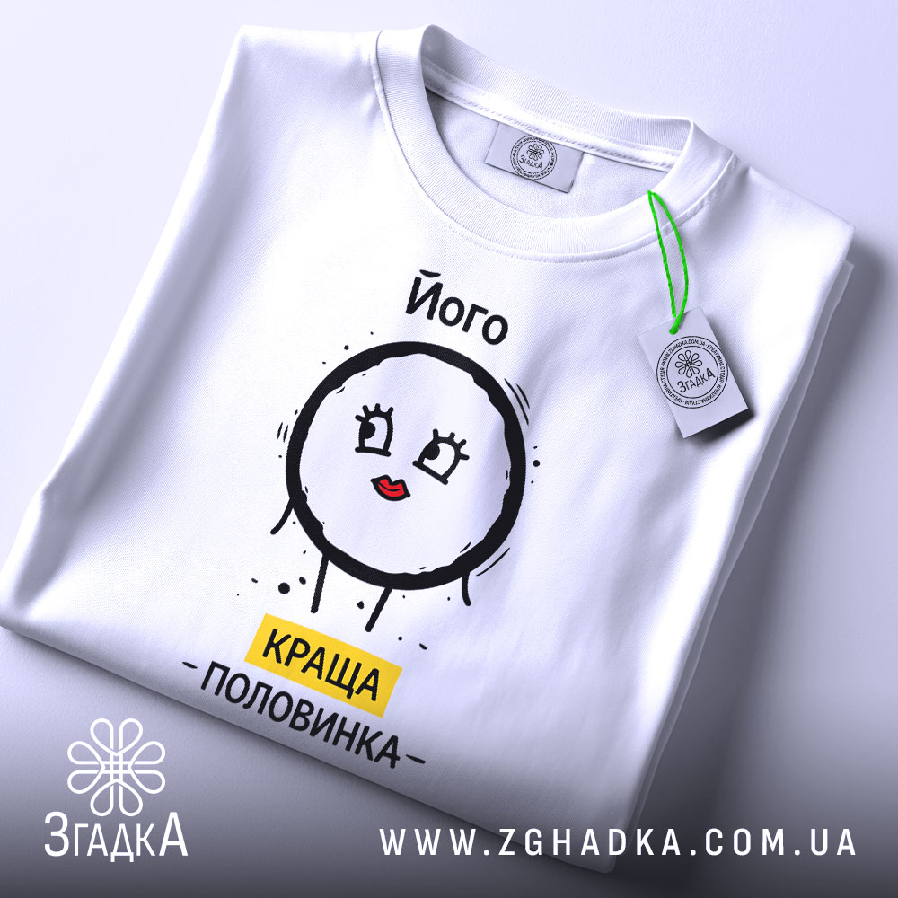 Футболка його краща половинка, білого кольору, складена на поверхні, фон світлий, принт з малюнком круглого персонажа з червоними губами та написом 'КРАЩА ПОЛОВИНКА' жовтого кольору, на комірці видна етикетка.