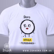 Футболка його краща половинка, білого кольору, складена на поверхні, фон світлий, принт з малюнком круглого персонажа з червоними губами та написом 'КРАЩА ПОЛОВИНКА' жовтого кольору, на комірці видна етикетка.