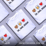 Футболка їж пий люби білого кольору, зображена на манекені, фон світло-сірий, принт складається з малюнків серця з піцою, пива в кружці та червоного серця, текст чорний, розташований під малюнками.