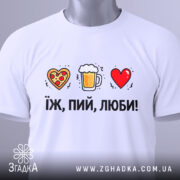 Футболка їж пий люби білого кольору, складена на поверхні, фон світло-сірий, принт з малюнками серця з піцою, пива в кружці та червоного серця, текст чорний, розташований під малюнками, на комірці є етикетка.