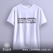 Футболка хороша дівчинка. Біла футболка на вішалці, з коротким рукавом, з текстом чорного кольору, що розташований по центру. Фон світлий, без додаткових елементів.