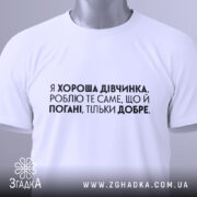 Футболка хороша дівчинка. Біла футболка, складена на поверхні, з коротким рукавом. На футболці чорний принт з текстом, на фоні світлого кольору, з зеленим ярликом.