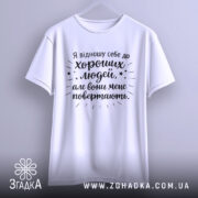 Футболка хороші люди, біла, підвішена на вішалці, фон світло-сірий, принт чорного кольору з текстом та зірочками.