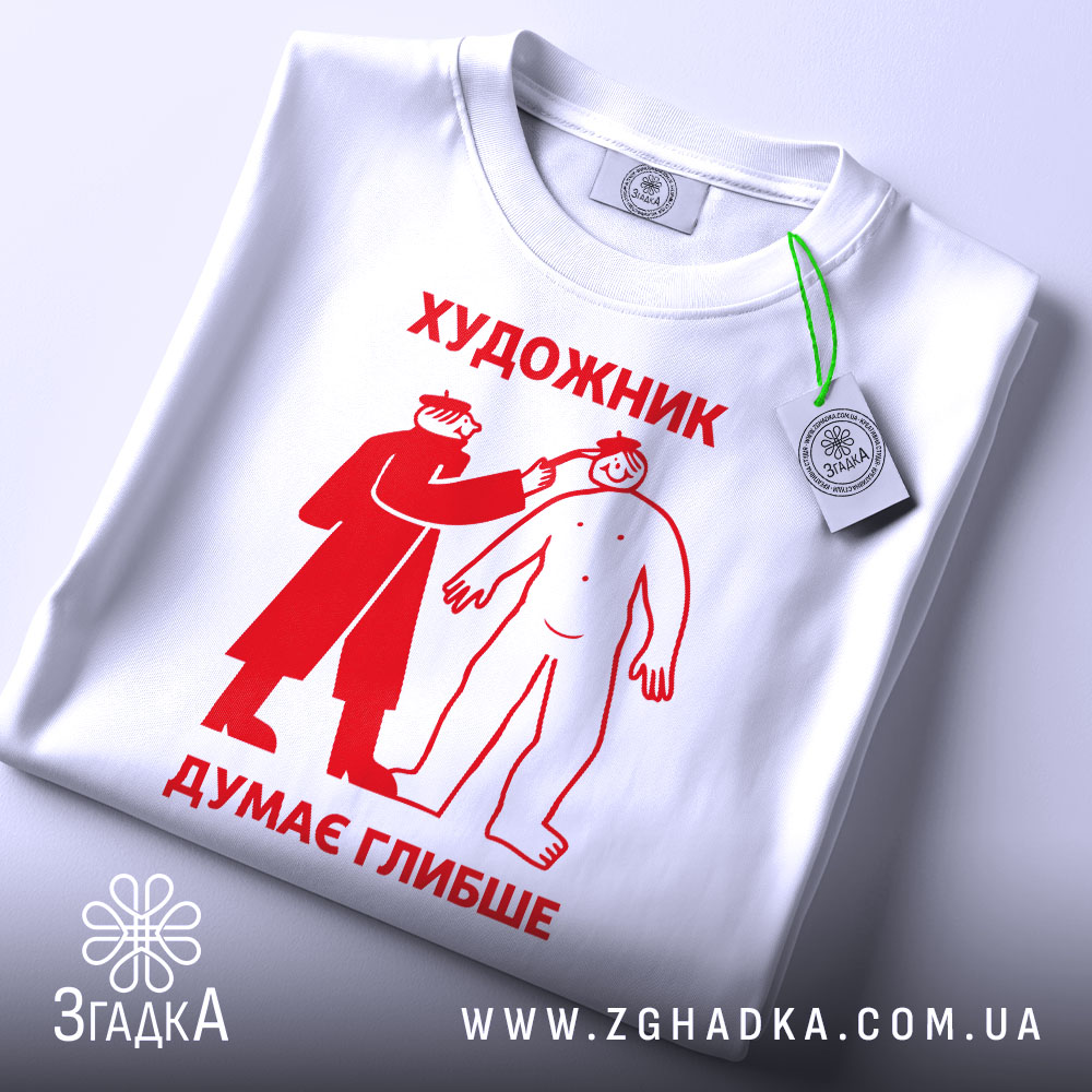 Футболка художник думає глибше, біла, зображена зверху, на столі, фон світло-сірий, принт червоного кольору з малюнком художника, що малює людину, з етикеткою на зеленому шнурку.