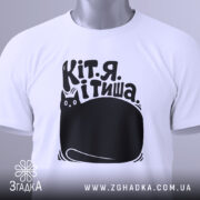 Футболка Кіт я тиша. Біла футболка з коротким рукавом, розкладена на поверхні. Принт чорного кольору з малюнком кота та текстом на українській мові видно чітко. На футболці є етикетка з зеленим шнурком. Фон світлий, однорідний.