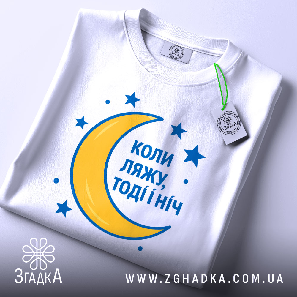 Футболка коли ляжу, біла, складена на поверхні, фон світло-сірий, принт з жовтою місяцем та синіми зірками, текст синій, з етикеткою.