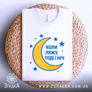 Футболка коли ляжу, біла, складена на кошику, фон світло-сірий, принт з жовтою місяцем та синіми зірками, текст синій.