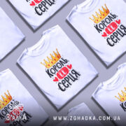 Футболка король її серця, білого кольору, зображена на манекені з правого ракурсу, фон світло-сірий, принт з короною, червоними сердечками та написом чорного кольору.