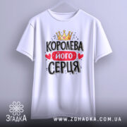 Футболка королева його серця, біла, підвішена на вішалці, фон світло-сірий, принт з короною, червоним написом і сердечками.