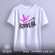 Футболка королева білого кольору, підвішена на вішалці, фон світло-сірий, принт з фіолетовою короною та чорним написом 'КОРОЛЕВА' з крапельками.