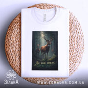 Футболка ліс знає ким я є, біла, зображена зверху на плетеній основі, на фоні світлого кольору, принт з оленями в лісі, текст на українській мові.