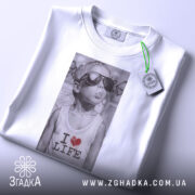 Футболка люблю життя, біла, з верхнього ракурсу, складена на поверхні, принт з зображенням хлопчика в сонцезахисних окулярах, текстом 'I ❤️ LIFE', з етикеткою на шнурку.