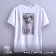 Футболка люблю життя, біла, з бокового ракурсу, підвішена на вішалці, принт з зображенням хлопчика в сонцезахисних окулярах, текстом 'I ❤️ LIFE'.