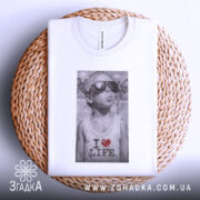 Футболка люблю життя, біла, з верхнього ракурсу, складена на плетеній основі, принт з зображенням хлопчика в сонцезахисних окулярах, текстом 'I ❤️ LIFE'.