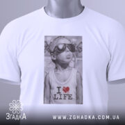 Футболка люблю життя, біла, з верхнього ракурсу, складена на поверхні, принт з зображенням хлопчика в сонцезахисних окулярах, текстом 'I ❤️ LIFE', з етикеткою на шнурку.