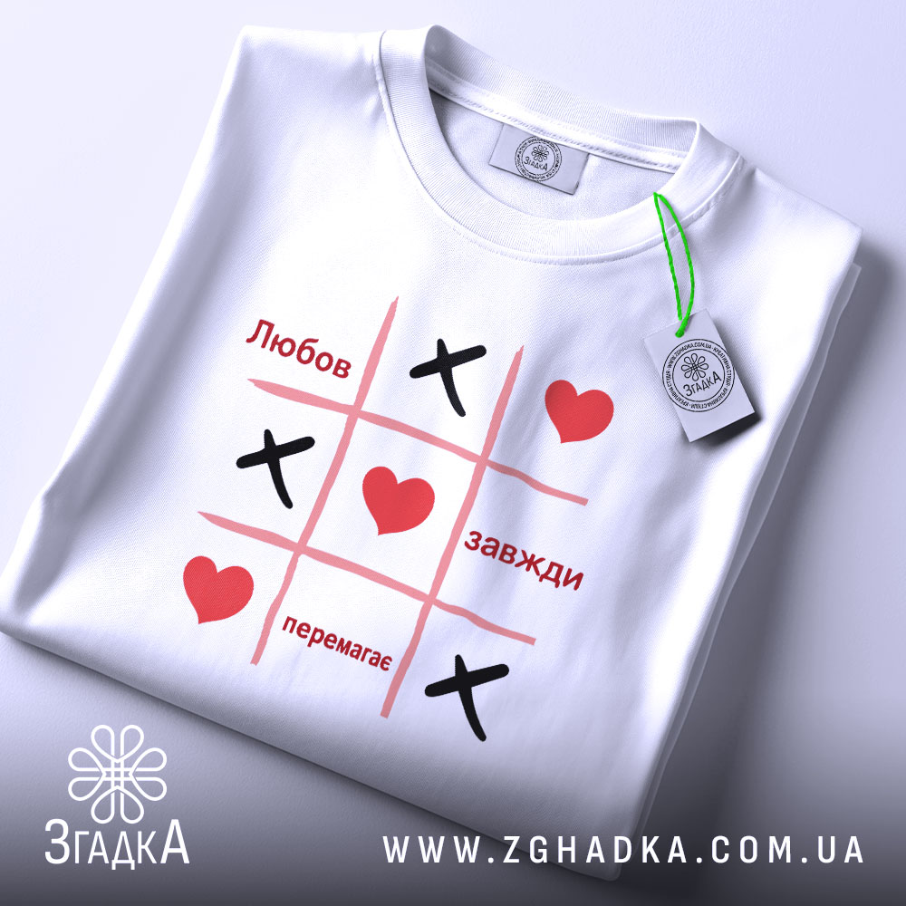 Футболка любов завжди перемагає, складена футболка білого кольору з принтом у стилі гри "Хрестики-нулики", на ній видно червоні серця та чорні "Х", фон світло-блакитний, ракурс зверху.