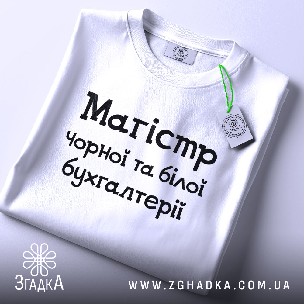 Футболка магістр чорної бухгалтерії, білого кольору, складена на поверхні, фон світло-сірий, принт чорного кольору з текстом 'Магістр чорної та білої бухгалтерії', на комірці видна етикетка.