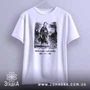 Футболка мій темп мій вибір. Біла футболка з коротким рукавом, підвішена на вішалці. На ній чорний принт з чоловіком у традиційному одязі, що йде по вулиці. Текст під зображенням чорного кольору. Фон світлий, з легким градієнтом.