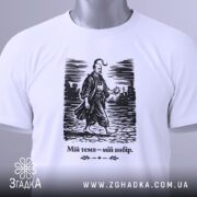 Футболка мій темп мій вибір. Біла футболка, зображена зверху, з коротким рукавом, на ній принт з чоловіком у традиційному одязі, що йде по вулиці. Принт чорного кольору, текст під ним також чорний. На футболці видно етикетку з зеленим шнурком.