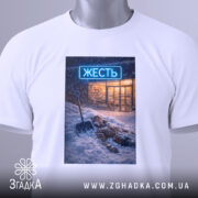 Футболка міська жесть, біла, складена на столі, фон світло-сірий, принт з зображенням людини, що лежить у снігу з лопатою, на фоні магазину з неоновим написом 'ЖЕСТЬ', на футболці є етикетка з зеленим шнурком.