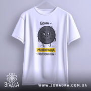 Футболка моя краща половинка, білого кольору, підвішена на вішалці, фон світло-сірий, принт з персонажем у вигляді печива Oreo, напис 'Вона - моя краща половинка' жовтого кольору, видно округлі краї рукавів.