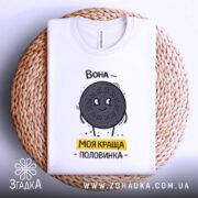 Футболка моя краща половинка, білого кольору, складена на плетеному кошику, фон світло-сірий, принт з персонажем у вигляді печива Oreo, напис 'Вона - моя краща половинка' жовтого кольору, видно округлий виріз горловини.