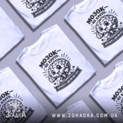 Футболка мозок це круто. Біла футболка з коротким рукавом, зображена з фронтального ракурсу на манекені. На футболці чорний принт з веселим мозком, що піднімає великий палець, та написом 'МОЗОК - ЦЕ КРУТО'. Фон світлий, з плавними градієнтами.