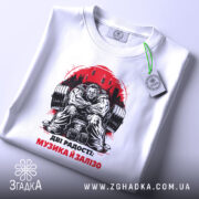 Футболка музика і залізо: біла футболка з принтом, зображення чоловіка з важкими гирями, ракурс зверху, на футболці є етикетка з зеленим шнурком, фон світлий.