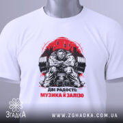 Футболка музика і залізо: біла футболка з принтом, зображення чоловіка з важкими гирями, ракурс зверху, на футболці є етикетка з зеленим шнурком, фон світлий.