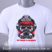 Футболка музика та штанги, біла, зображена зверху, фон світло-сірий, принт з чорним і червоним кольорами, атлет з штангою та написом 'Мені достатньо двох речей: музики та штанги', з зеленим ярликом.