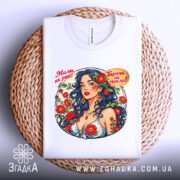 Футболка мила як рай. Біла футболка, складена на плетеному кошику, з яскравим принтом жінки з синім волоссям. Фон світлий, акцент на принті.