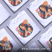 Футболка мила як рай. Біла футболка на манекені, з яскравим принтом, що зображує жінку з синім волоссям та квітами. Фон світлий, акцент на принті.