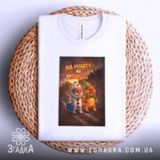 Футболка на роботу білого кольору, розкладена на плетеній основі, фон світлий, принт з двома персонажами, один у костюмі клоуна, інший у зеленому капелюсі, текст на принті: 'НА РОБОТУ – ЯК НА СВЯТО!'.