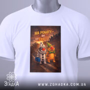 Футболка на роботу білого кольору, розкладена на поверхні, фон світлий, принт з двома персонажами, один у костюмі клоуна, інший у зеленому капелюсі, текст на принті: 'НА РОБОТУ – ЯК НА СВЯТО!', на футболці є етикетка з зеленим шнурком.