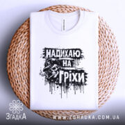 Футболка надихаю на гріхи, біла, складена на плетеній кошику, фон світлий, принт чорного кольору з черепом у капелюсі, виглядає затишно і привабливо.