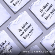 Футболка не бійся бажань. Біла футболка з коротким рукавом, зображена з правого ракурсу на манекені, фон світло-сірий, принт чорного кольору з текстом "Не Бійся своїх бажань! Бійся моїх!".