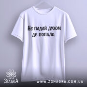 Футболка не падай духом, білого кольору, підвішена на вішалці, фон світло-сірий, принт чорного кольору з текстом 'Не падай духом де попало.'