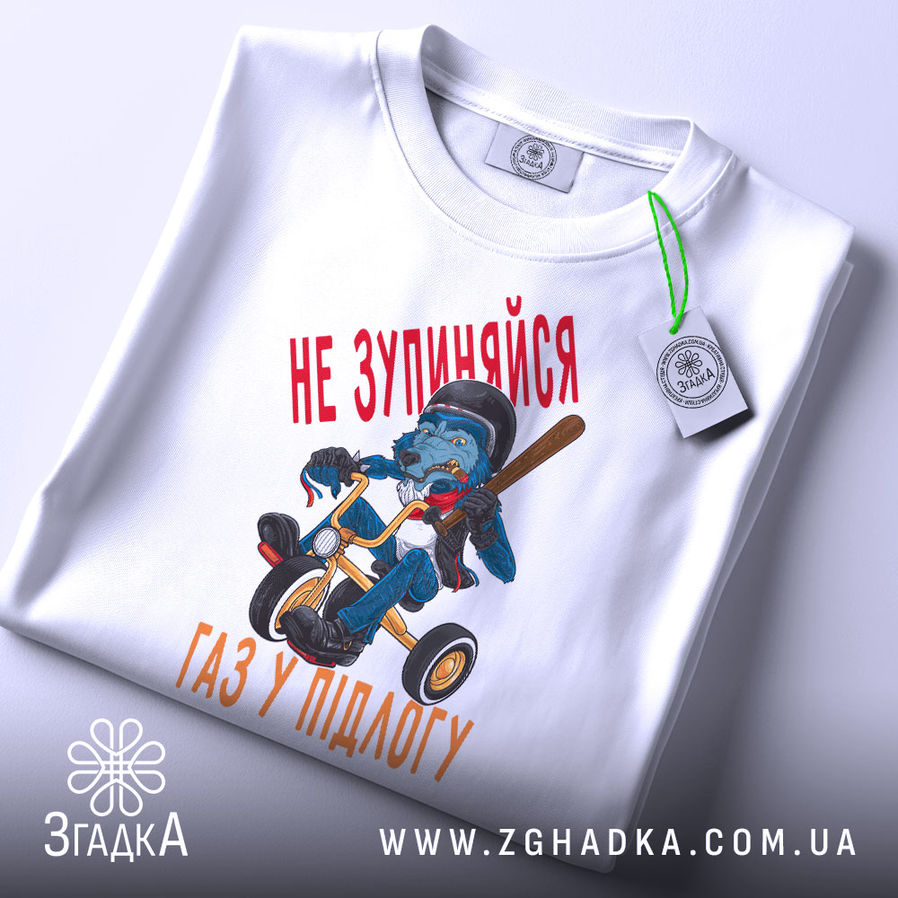 Футболка не зупиняйся, біла, зображена зверху, на ній видно етикетку, фон світло-сірий, принт з малюнком ведмедя на триколісному велосипеді з червоним текстом 'НЕ ЗУПИНЯЙСЯ' та 'ГАЗ У ПІДЛОГУ'.