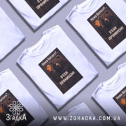 Футболка нема батога. Біла футболка з коротким рукавом, зображена з фронтального ракурсу на манекені. На фоні світло-сірий градієнт. Принт з ведмедем, який тримає пряник у формі черепа, з текстом на українській мові.