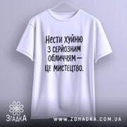 Футболка нести хуйню, білого кольору, підвішена на вішалці, фон світлий, принт чорного кольору з текстом: 'Нести хуйню з серйозним обличчям – це мистецтво.'