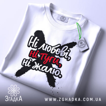 Футболка ні любові, біла, зображена зверху, складена на поверхні, фон світлий, принт чорного кольору з червоними акцентами, текст "Ні любові, ні туги, ні жалю" чітко видимий, на футболці є етикетка з зеленим шнурком.