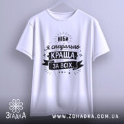 Футболка ніби я краща, білого кольору, підвішена на вішалці, фон світло-сірий, принт чорного кольору з текстом "Ніби я спеціально краща за всіх" та декоративними елементами.