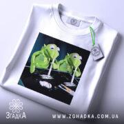 Футболка ніч без сну, біла, з верхнього ракурсу, складена, з етикеткою, на принті дві зелені ляльки, що тримають трубочки, фон чорний.