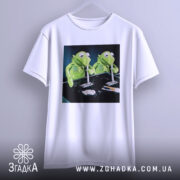 Футболка ніч без сну, біла, з прямим ракурсом, підвішена на вішалці, з принтом двох зелених ляльок, фон темний.