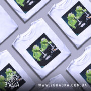 Футболка ніч без сну, біла, з прямим ракурсом, на манекені, з принтом двох зелених ляльок, що сидять за столом з чорним фоном.