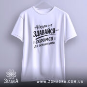 Футболка ніколи не здавайся, білого кольору, підвішена на вішалці, фон світло-сірий, принт чорного кольору з текстом 'Ніколи не здавайся—соромся до останнього'.