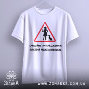 Футболка офіційне попередження: біла футболка з коротким рукавом, підвішена на вішалці, фон світло-сірий, принт у вигляді червоного трикутника з жінкою та котом, текст чорного кольору.