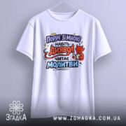 Футболка поруч зі мною, білого кольору, підвішена на вішалці, принт з червоним дияволом, який читає молитви, фон світло-сірий, ракурс спереду.