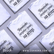 Футболка потрібні гроші. Біла футболка на манекені, з коротким рукавом, на світлому фоні. Принт чорного кольору з текстом "Терміново потрібні гроші: на вітер" розташований по центру.